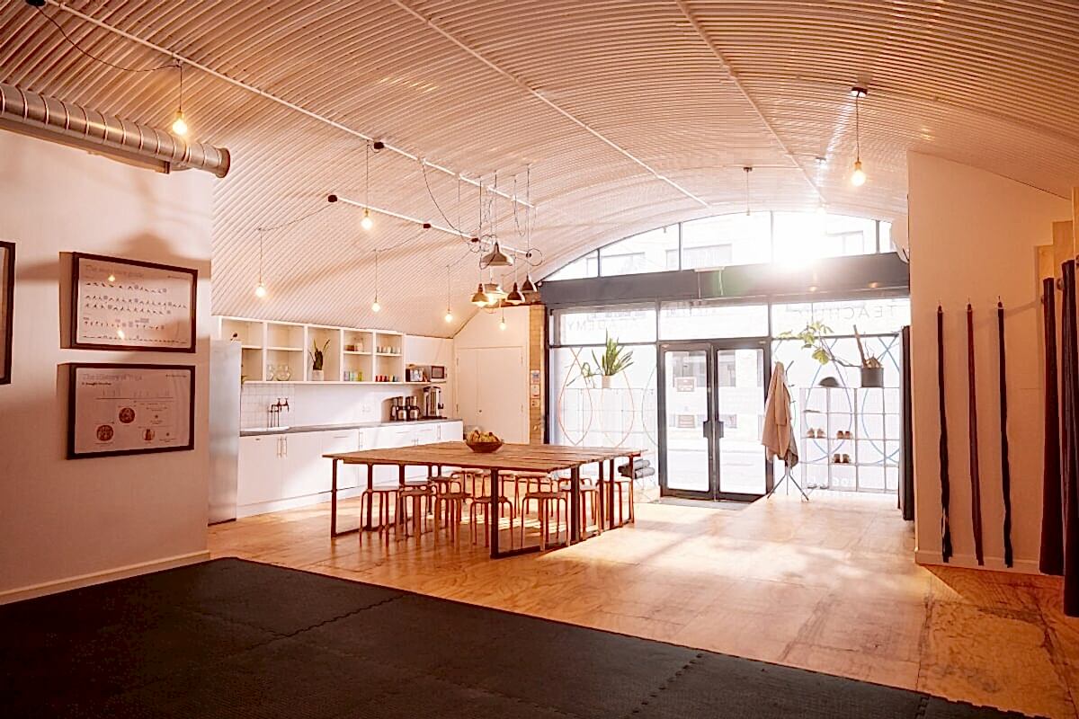 The interior of the Hotpod Yoga Teacher Academy with pendant lights, large glass windows, a communal table and yoga matts