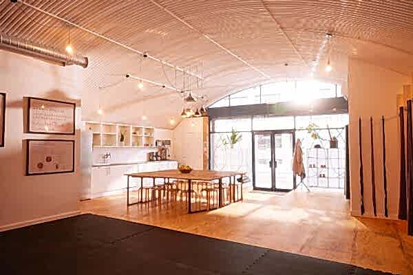 The interior of the Hotpod Yoga Teacher Academy with pendant lights, large glass windows, a communal table and yoga matts